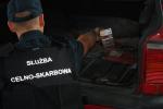 Funkcjonariusz służby celno-skarbowej wyjmuje przemycane papierosy ze skrytki w samochodzie