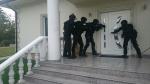 Zdjęcie przedstawia trzech funkcjonariuszy z bronią wchodzących do budynku