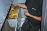 Zdjęcie przedstawia funkcjonariusza Służby Celno-Skarbowej, który wykrył i trzyma w ręku nielegalne paczki papierosów. 