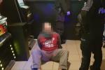 Na zdjęciu siedzący na podłodze człowiek zakuty w kajdanki i funkcjonariusze KAS