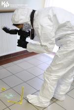 Kobieta, technik kryminalistyki w kombinezonie fotografuje ślady.