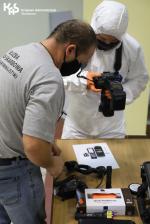 Instruktor, technik kryminalistyki Służby Celno-Skarbowej wraz z uczestnikiem szkolenia pochylają się nad stołem z dowodami.