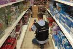 Korytarz sklepowy. Funkcjonariusz Służby Celno-Skarbowej robi zdjęcie zabawkom ułożonym na regałach sklepowych.