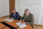 Dyrektor Izby Administracji Skarbowej w Olsztynie i Dyrektor Regionalnej Dyrekcji Lasów Państwowych w Olsztynie siedzą za stołem i podpisują dokumenty. 