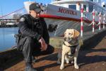 Funkcjonariusz z psem służbowym pozują do zdjęcia przy statku.