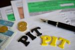 Formularze PIT, banknoty 50 złotowe oraz monety - grosze, pióro na kartce papieru oraz dwa napisy PIT.
