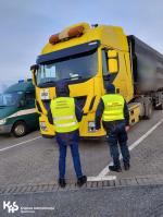 Funkcjonariusz Służby Celno-Skarbowej i inspektor Wojewódzkiego Inspektoratu Ochrony Środowiska stoją przed kabiną ciężarówki.