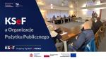 Napis: KSeF Krajowy System e-Faktur a Organizacje Pożytku Publicznego. Zdjęcie grupy osób w sali konferencyjnej. Dwóch prowadzących spotkanie stoi przy ekranie rzutnika oraz rollupie Krajowej Administracji Skarbowej.