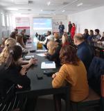 Sala szkoleniowa. Uczestnicy siedzą. Troje szkolących stoi przed nimi. 