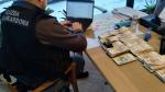 Funkcjonariusz siedzi przy laptopie, który znajduje się na biurku, obok poukładane kupki z banknotami