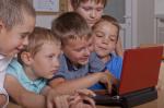Na zdjęciu pięcioro dzieci siedzących przed laptopem
