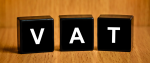 Grafika przedstawia trzy klocki, na których zamieszczone są pojedyncze litery tworzące napis VAT.